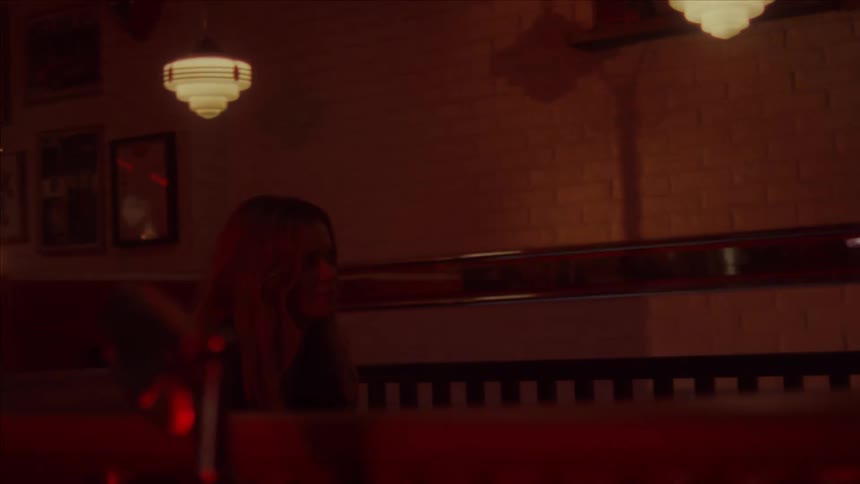 A woman sits in a booth at a dimly lit diner with flickering lights as another woman comes to sit across from her