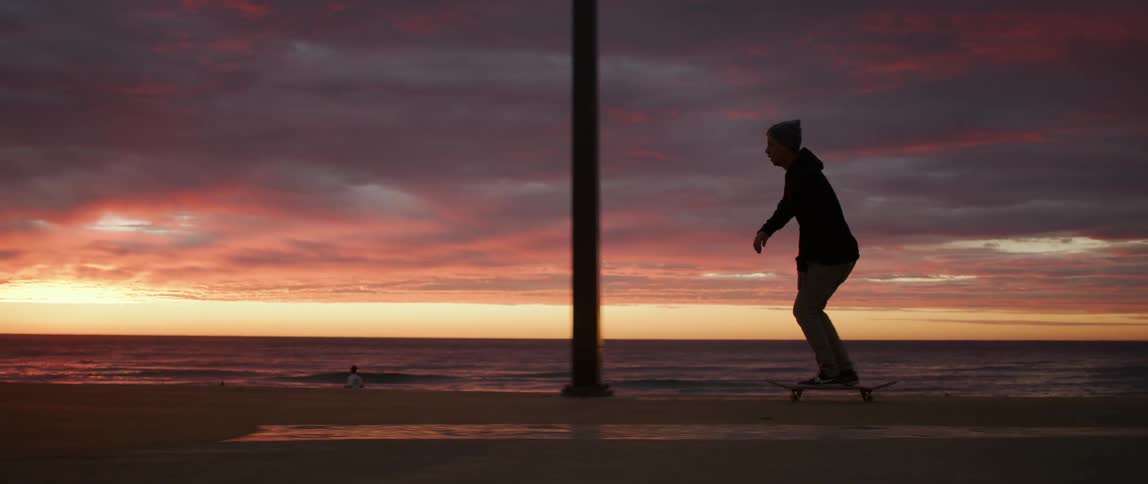 A silhouetted skateboarder riding on a beach at sunset