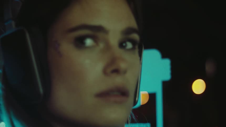 A woman with headphones looking at her reflection on a glass window