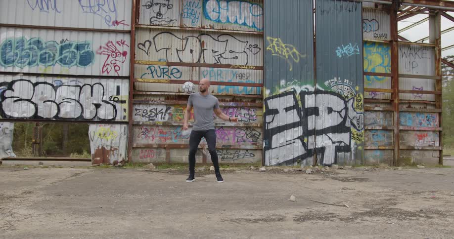 A man juggles a soccer ball with his legs while standing outdoors during the day