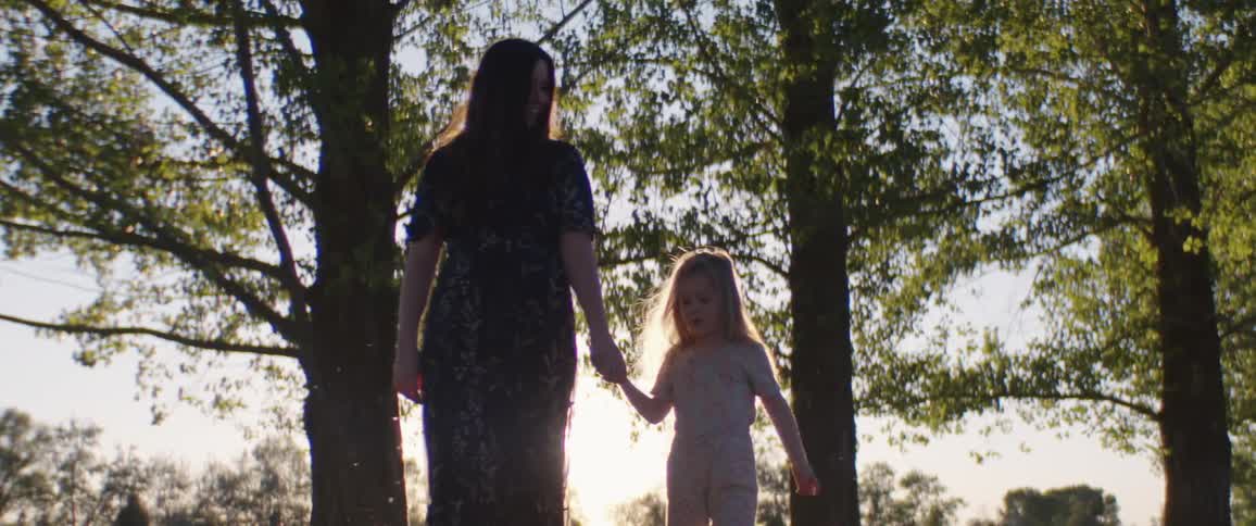 A mother walks through a field while holding hands with her daughter during the day