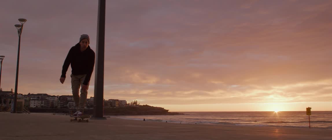 A man rides a skateboard along the coast of a city at sunset