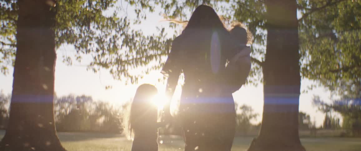 A mother and two daughters walking into a beautiful park with cotton flying everywhere