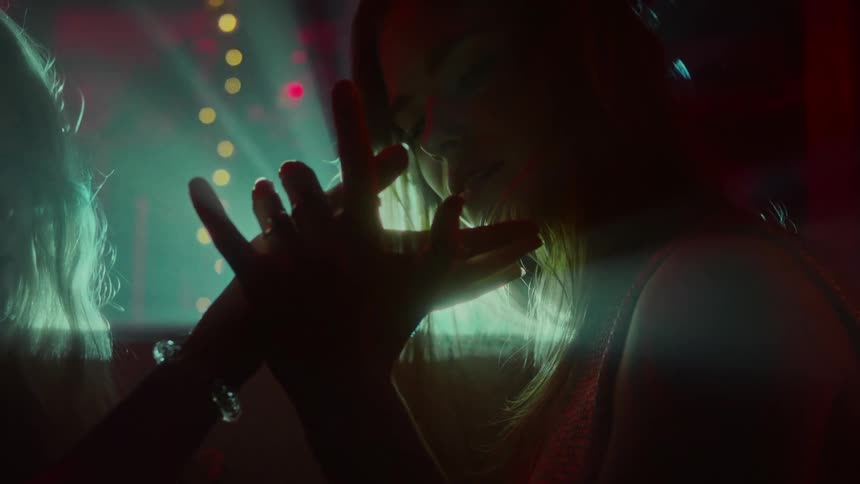 Two women in a nightclub holding hands with a spotlight and a wall in the background
