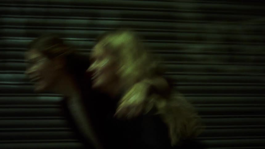 A pair of women laugh and hug each other while they run down a city sidewalk together at night