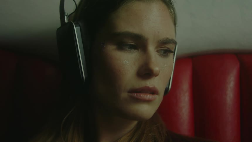 A concerned looking woman wearing headphones while sitting on a red chair