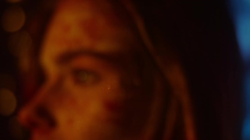 A woman with glittery makeup looks to the side as shadows are projected across her face