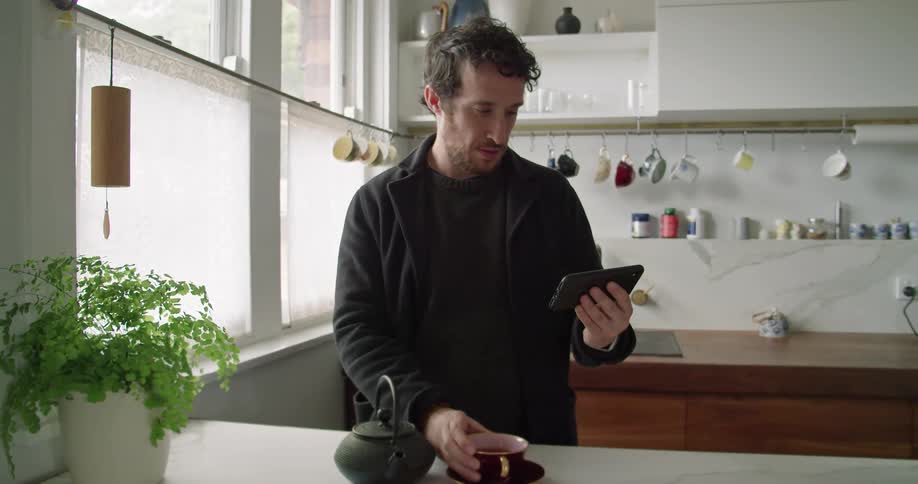 A man stands in his kitchen while talking to someone via video chat on his smart phone