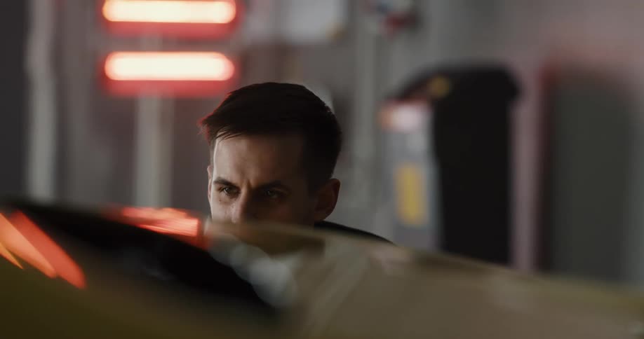 A man uses a cloth to polish the exterior of a car in a garage