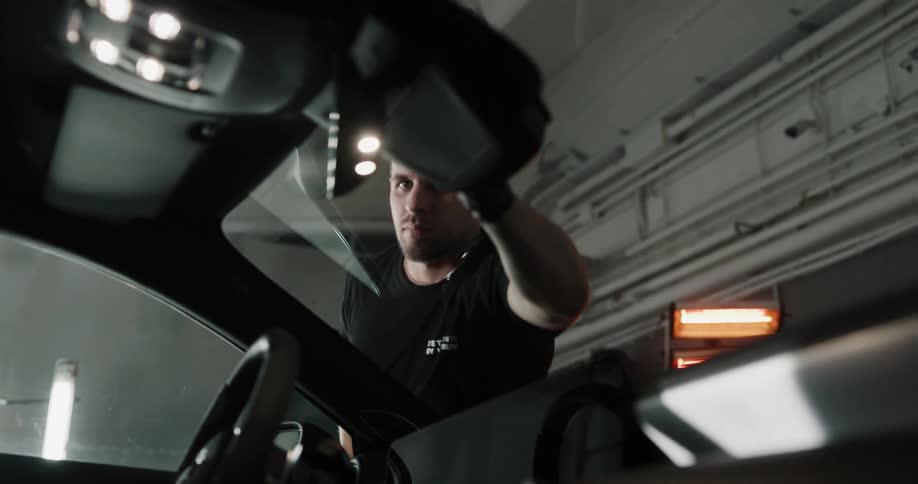 An employee at an auto detailer wipes down the windshield of a car