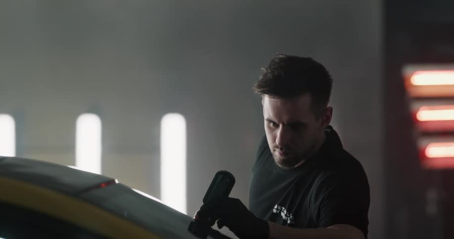 A man puts a cleaning product on a windshield inside a commercial garage