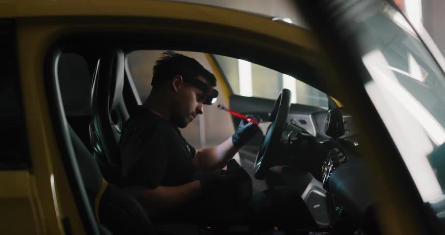 A man wearing a headlamp uses a brush and cloth to clean and detail a car