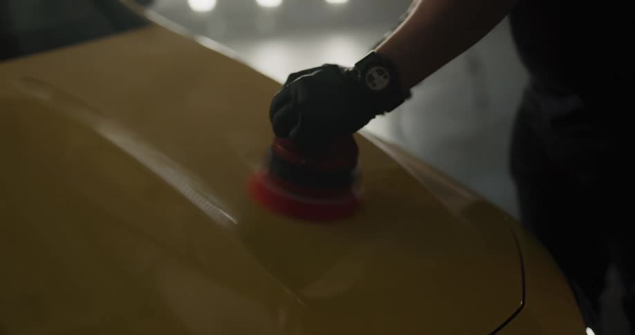 Man wearing gloves polishes the hood of a car with a polisher
