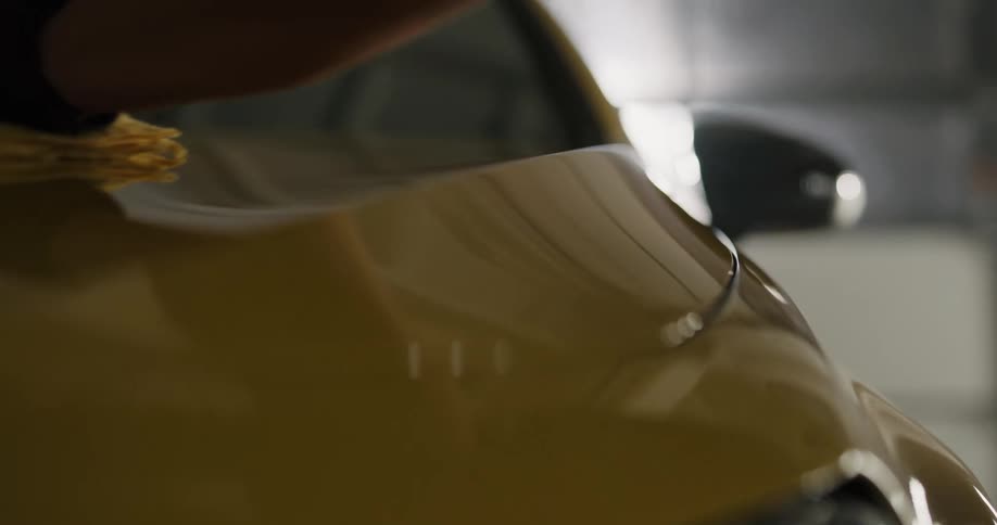 A man wearing gloves uses a microfiber cloth to shine and clean a car