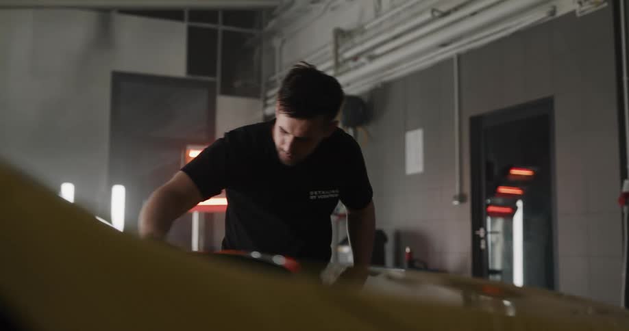 A man in a garage with a spray bottle and cloth cleaning a vehicle
