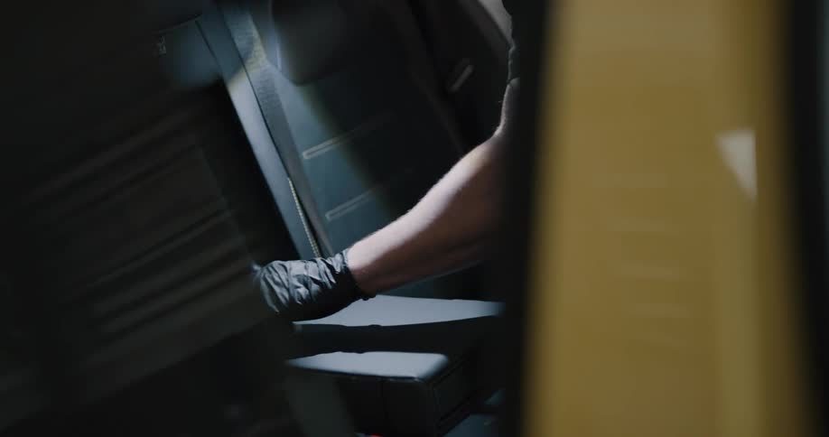A male car detailer scrubbing the backseat of a car with a cleaning brush