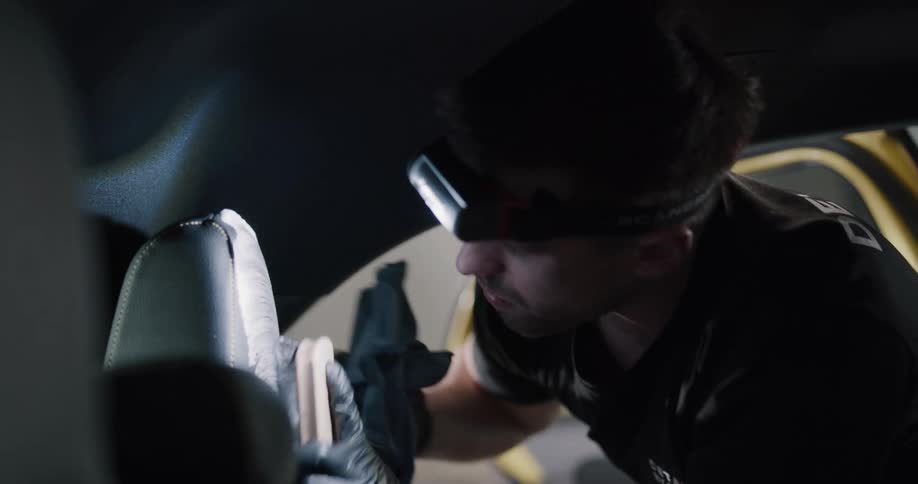 A man uses a foam and brush to clean the interior seat of a vehicle