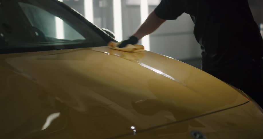A man shines a flashlight on the hood of a car while he cleans and shines it with a cloth