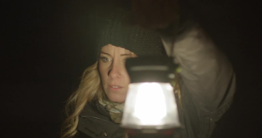 A blonde woman carries a lantern through a dark area
