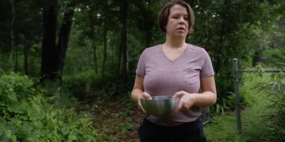 A woman walks in the yard with a bowl