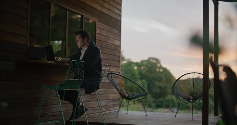 A man is sitting outdoors and typing on a laptop