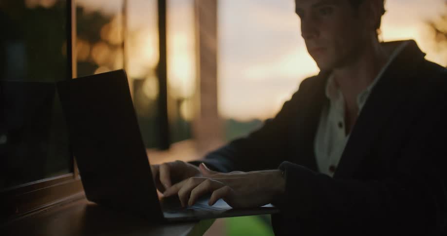 Man types on a laptop that is sitting on a ledge that is on the side of a building