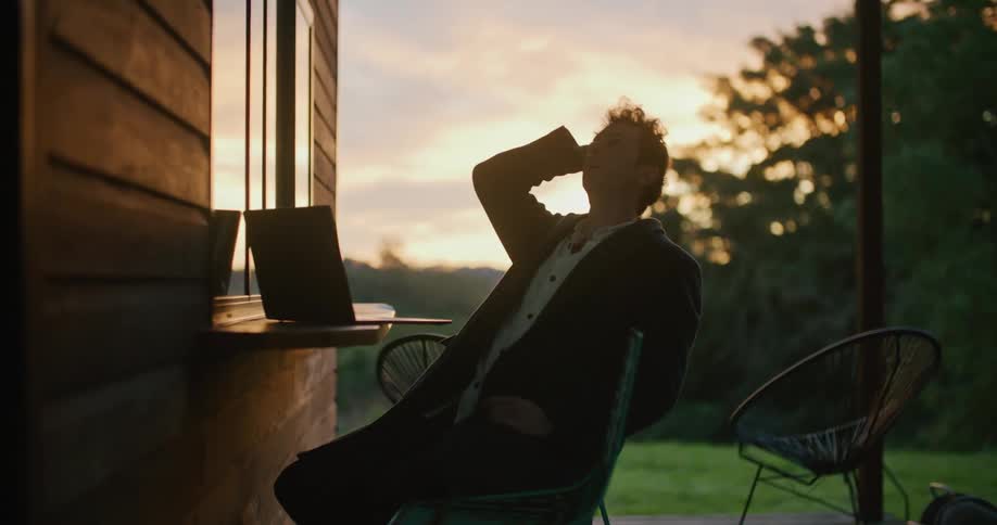 A man using a laptop with trees the sky and clouds in the background