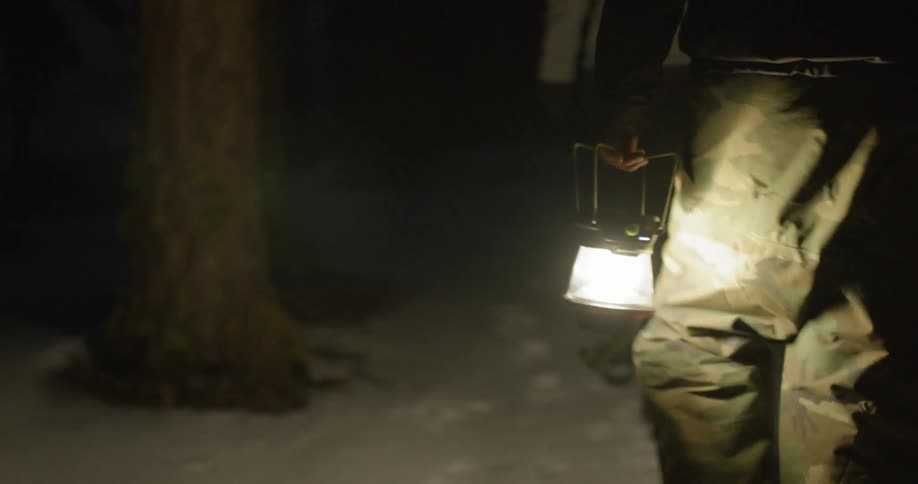 A man carries a lantern behind another person in the snow