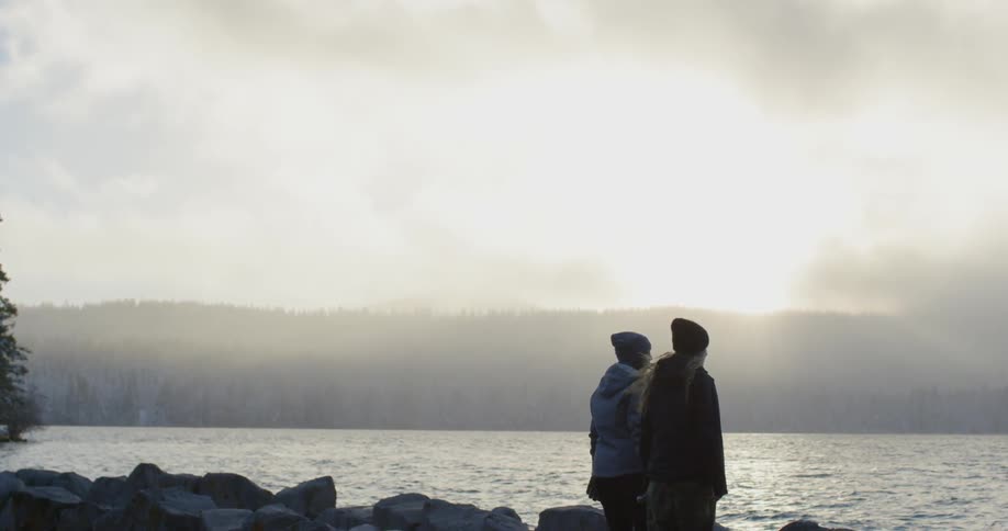 Two people on a rocky beach looking at the waters at sunset