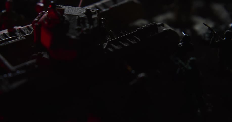 Soldier miniatures and tank figurine sitting on shadowed diorama are briefly lit by passing light