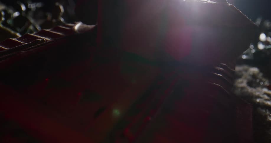 A bright light passes over a toy tank upside down in the dirt outside