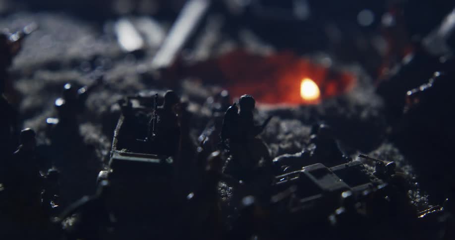 Toy soldiers are arranged around a burning flame in a makeshift trench