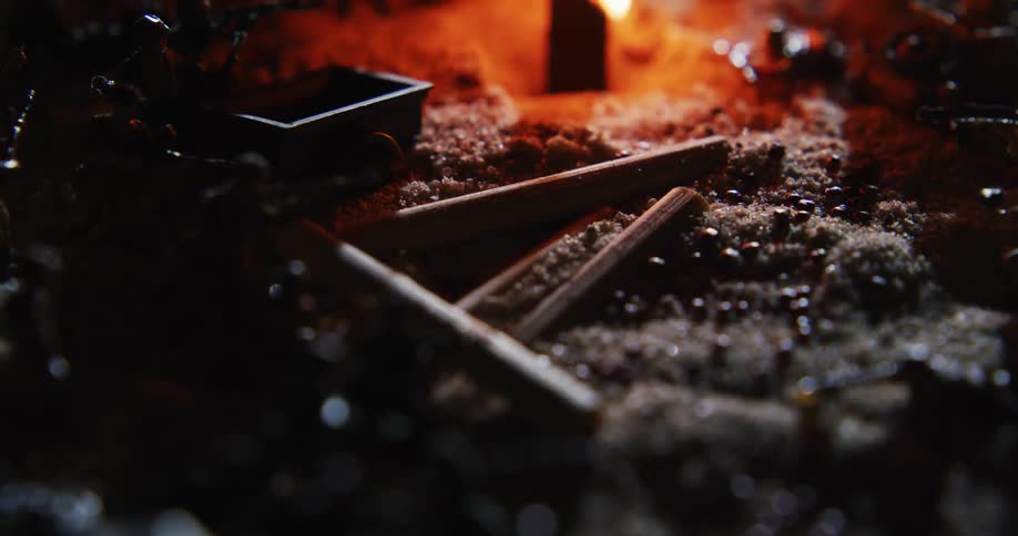 A pile of trash including a cigarette and pencils is shown on the grown with a fire lit in the background
