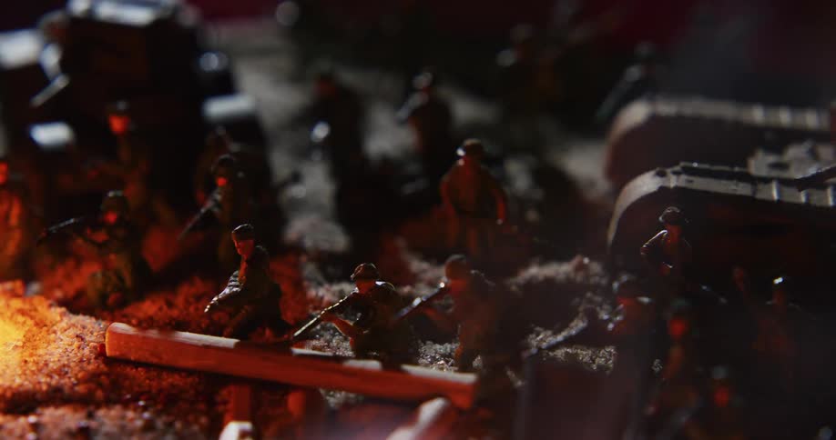 Small fires smoke in shadowy diorama of soldiers and tanks set on sandy terrain