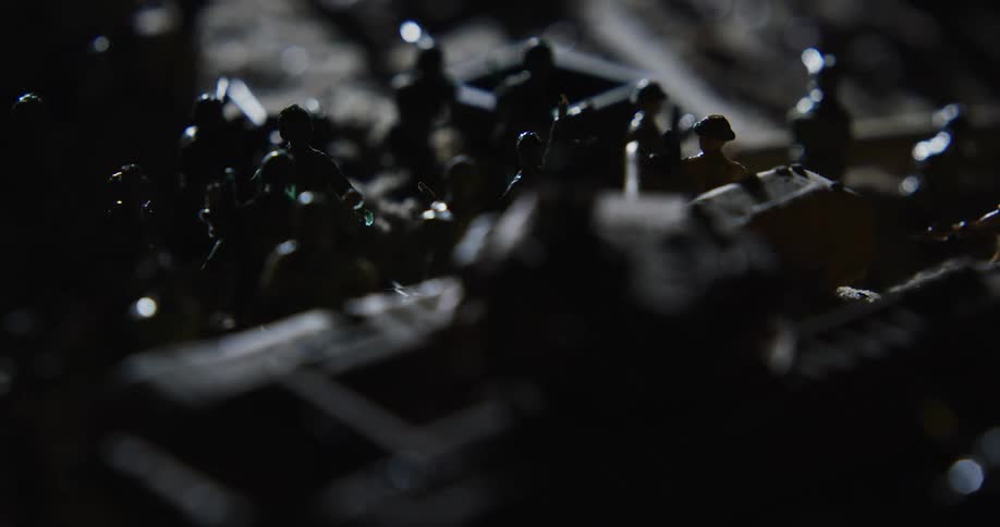 Soldier miniatures crowd together around tank figurine in shadows as light sweeps past