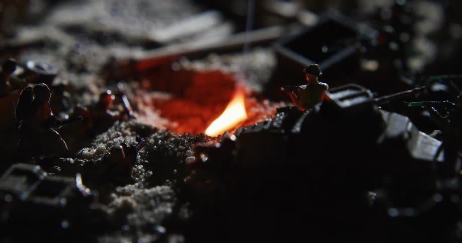 Fire burns in a hole surrounded by military toys