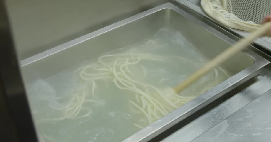 A restaurant cook stirs noodles in a big vat of water
