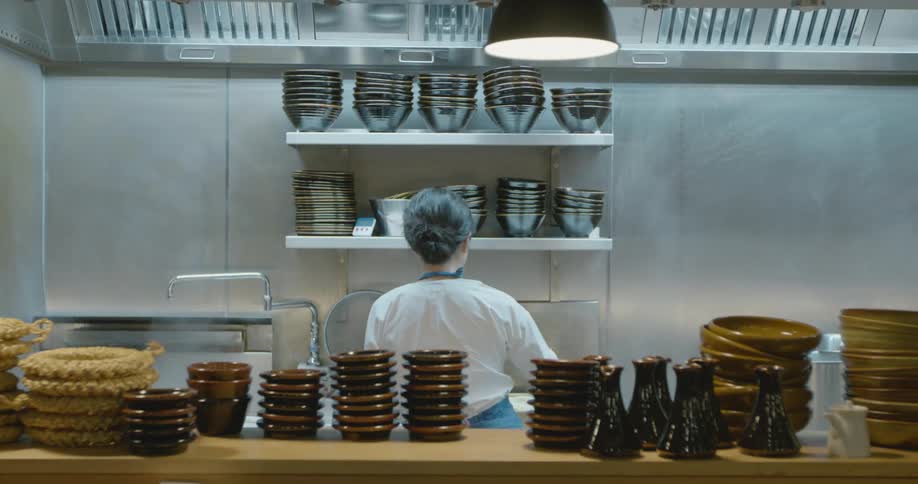 A female chef works in an industrial kitchen filled with steam