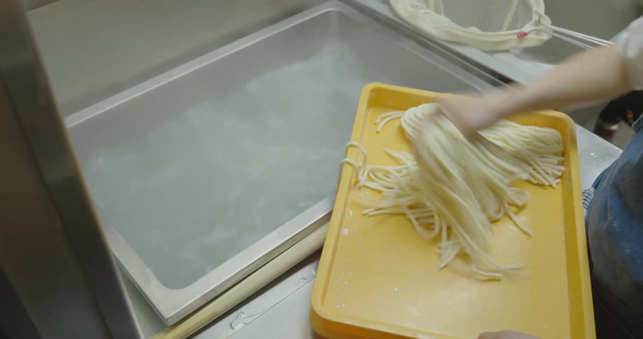 A person throwing raw noodles into a vat of boiling water inside a restaurant