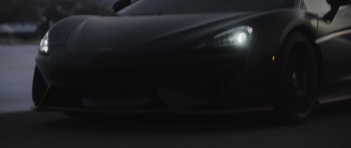 Black performance car speeds along road bordered by snow with mist covered mountains in background