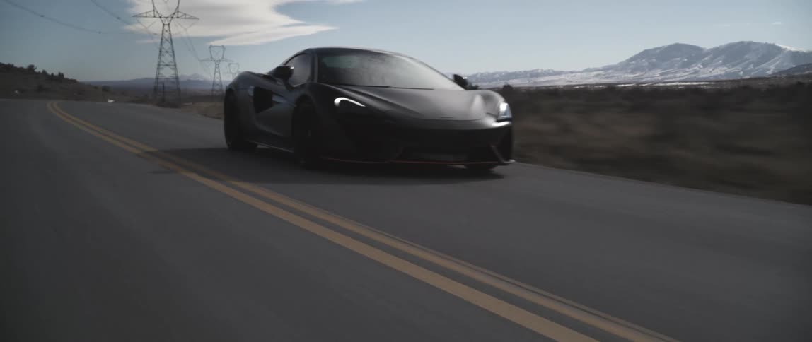 Black sports car drives along road paralleling power lines with mountains on horizon