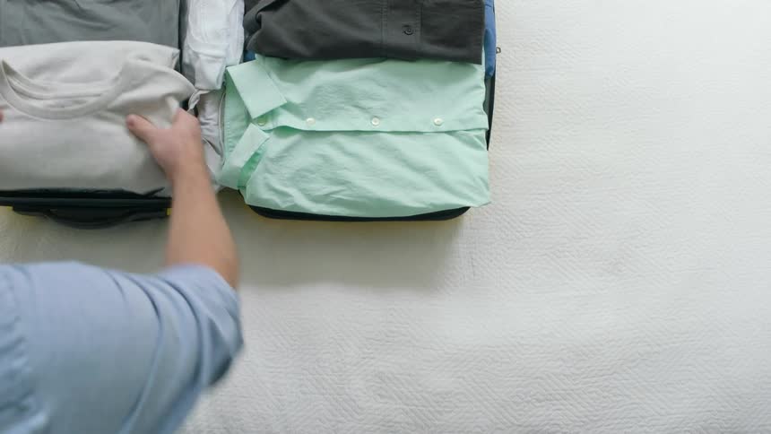 A man packing a suitcase full of clothes