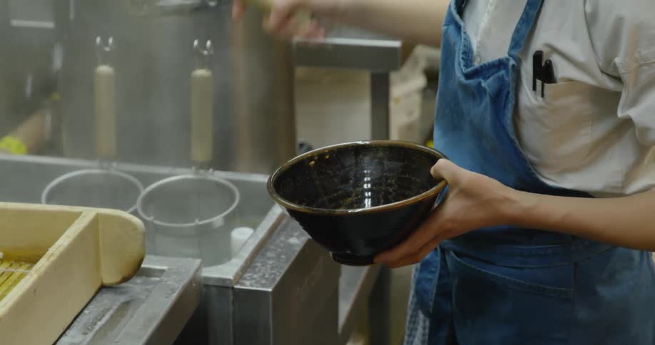 A cook shakes noodles in a strainer before pouring the noodles in a bowl