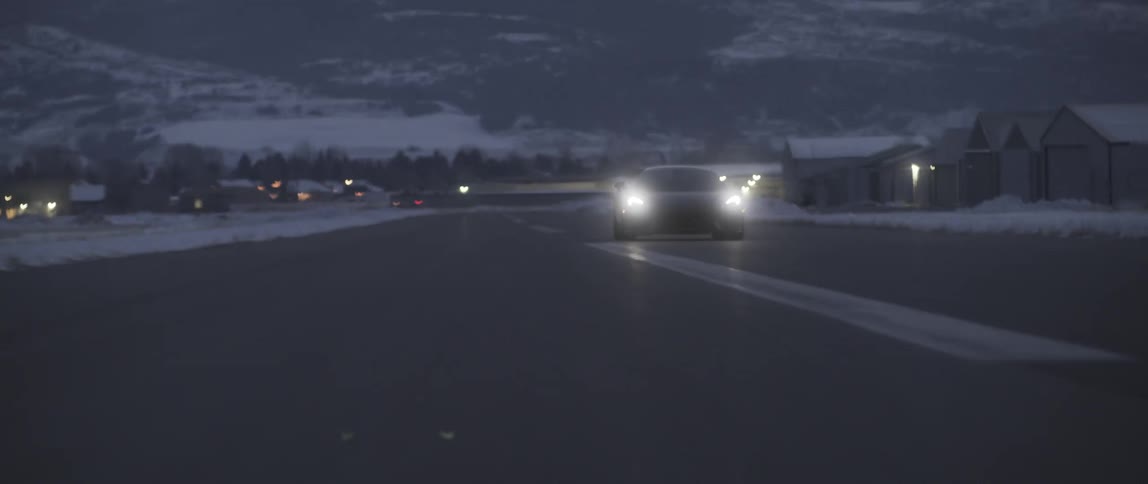 Sports Car speeds down road away from snow covered town at base of mountain under red tinted sky