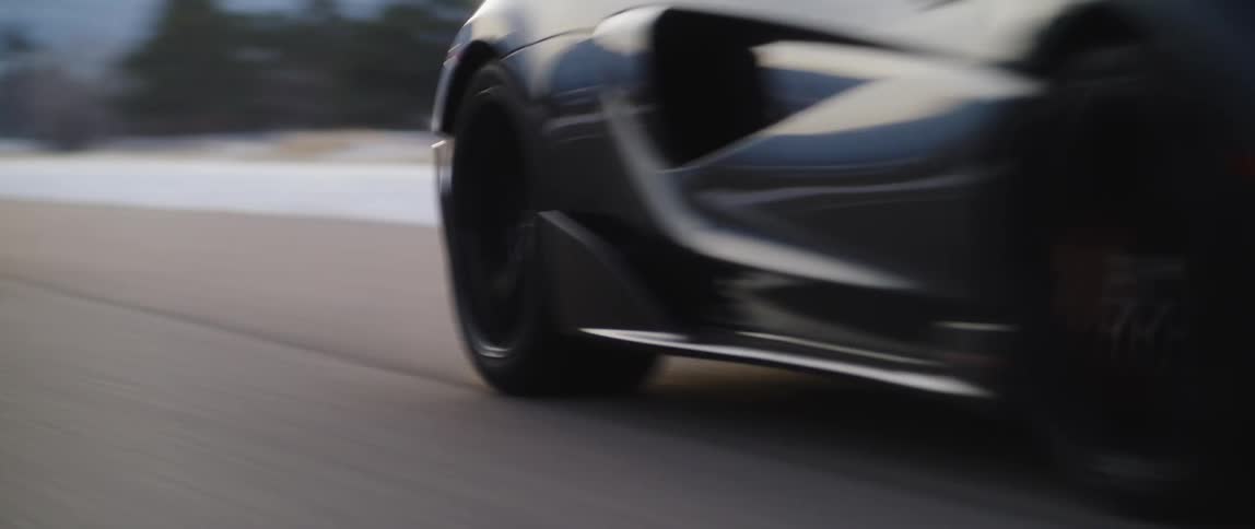 A sports car drives down a road with a snowy hill in the background