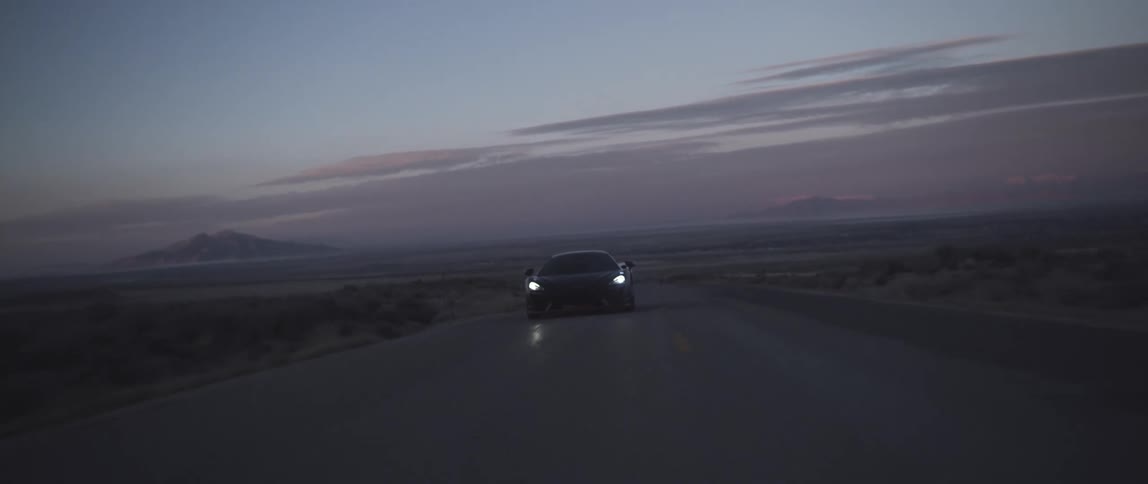 A sports car travels down a long road in the countryside in the evening