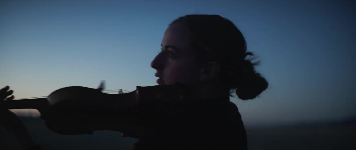A woman plays the violin outdoors as wind blows through her pulled back hair
