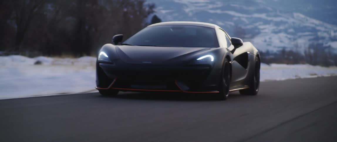 A black sports car speeds past snow covered mountains