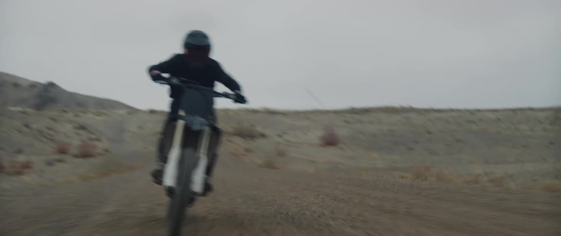 A person with a helmet riding a dirt bike on a dirt road with the sky and clouds in the background