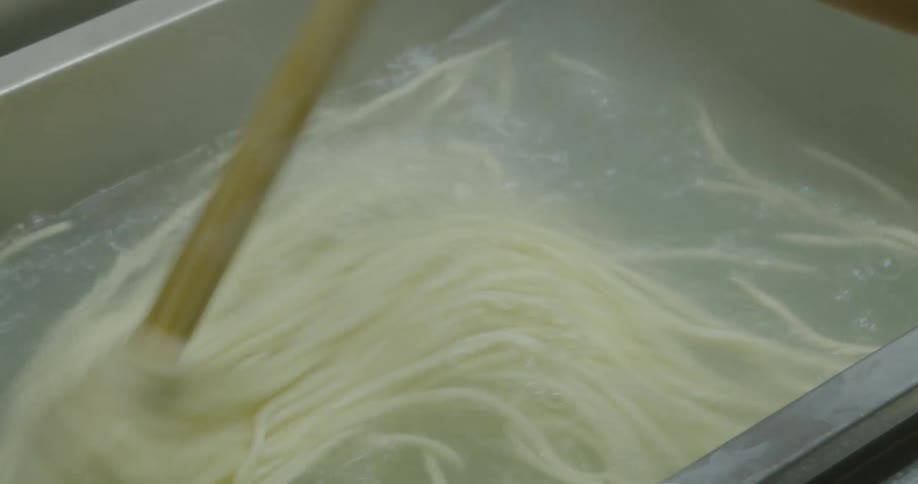 Pot of pasta being cooked in boiling water is stirred by a wooden stick